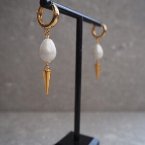 Närbild på guldfärgade örhängen med spikedetalj och droppformad pärla