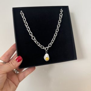 Närbild på halsband i rostfritt stål med chunky kedja och smiley-hänge i snäckskalspärla.