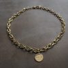 Minimalistiskt statement-halsband med rund berlock i mässing och graverat budskap.