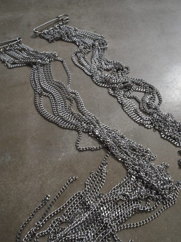 Brosch med säkerhetsnålar och långa kedjor i rostfritt stål fäst på kavaj